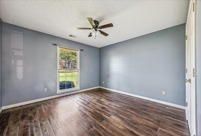 Spacious room featuring wood-finish flooring, a ceiling fan, and a double-hung window with exterior landscaping visible