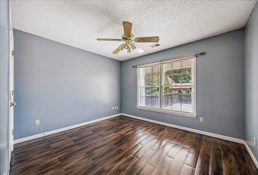 Spacious room featuring wood-finish flooring, a contemporary ceiling fan, and a large window with white trim overlooking an outdoor deck