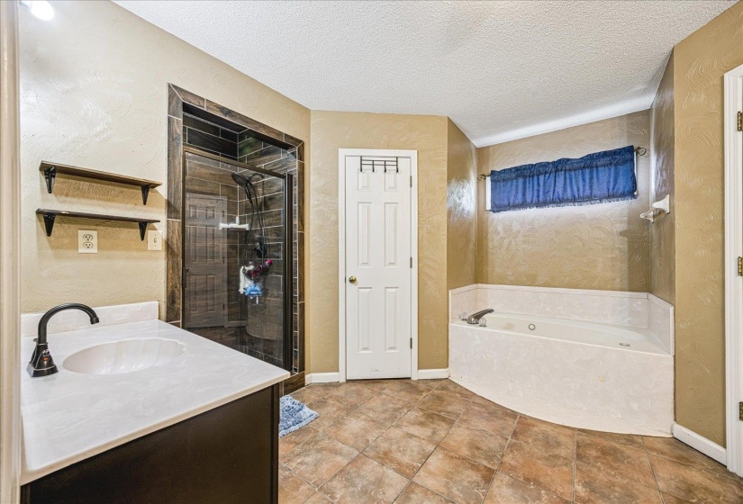 Spacious bathroom featuring a corner soaking tub, a walk-in shower with dark tile surround, and a vanity with an integrated sink and dark bronze faucet