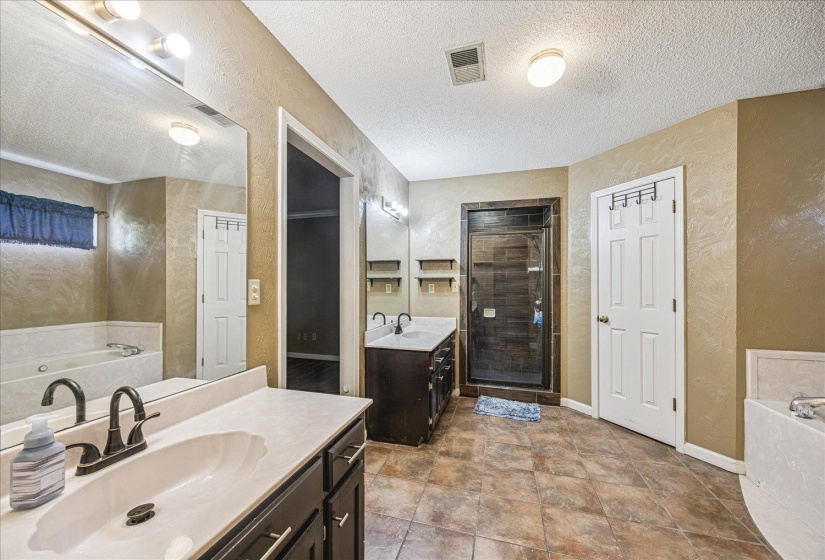 Bathroom featuring a dual vanity with dark wood-finish cabinetry, a framed glass shower, a built-in tub, and tile flooring