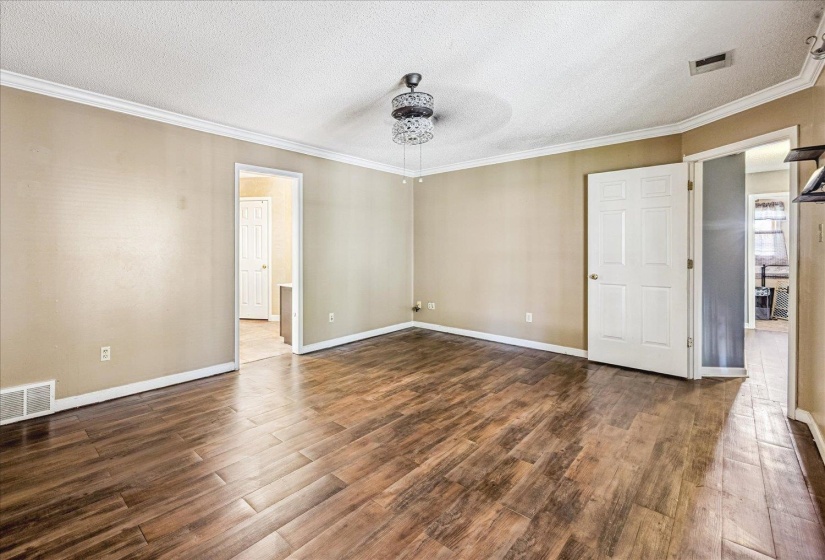Spacious room featuring wood-finish flooring, neutral-toned walls, and white crown molding