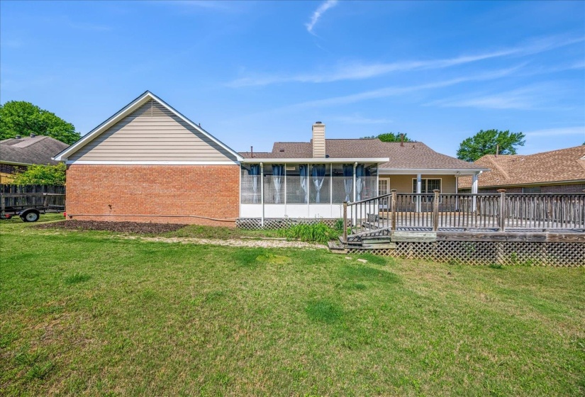 Expansive backyard featuring a large wooden deck, screened porch, brick exterior, and a manicured lawn