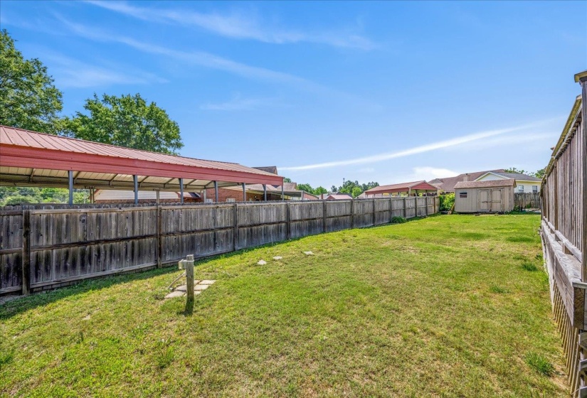 Expansive rear yard featuring a wooden privacy fence, a detached shed, and natural grass