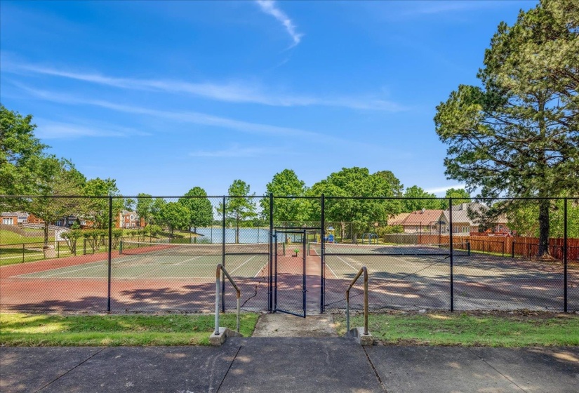 Hard-surfaced tennis courts featuring green and red playing areas, surrounded by chain-link fencing