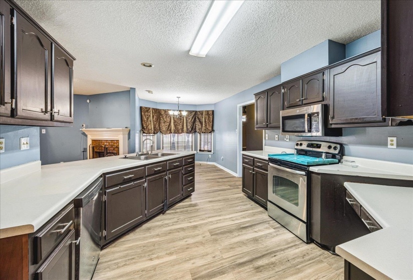 Kitchen featuring dark wood cabinetry, white countertops, stainless steel appliances, and wood-finish flooring