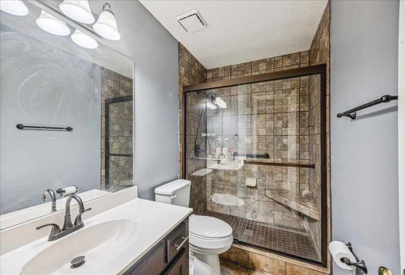 Walk-in shower with clear glass enclosure and stone-look tile surround