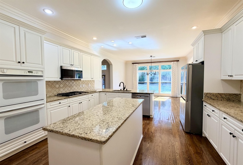 Gourmet kitchen with white cabinetry, granite countertops, tile backsplash, built-in double ovens, and wood-finish flooring