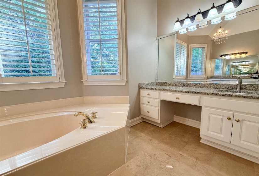 Soaking tub with brass fixtures, framed by two windows with plantation shutters