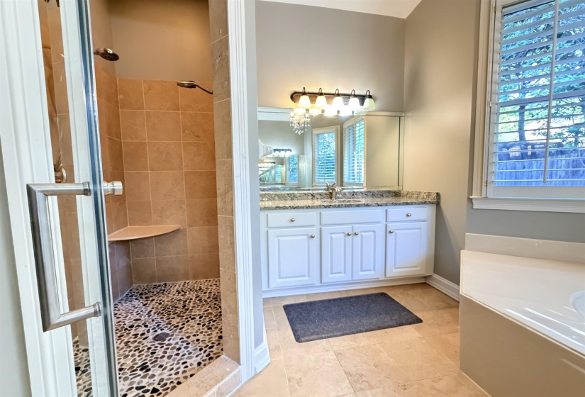 Walk-in shower with pebble tile flooring and a built-in corner bench