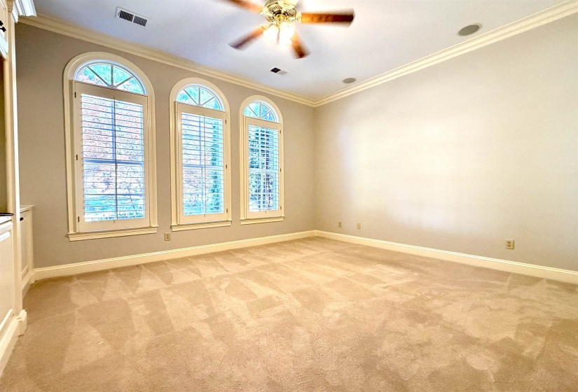 Spacious room featuring three arched windows with plantation shutters, crown molding, built-in cabinetry, and neutral-toned carpeting