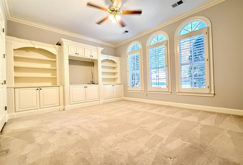 Room featuring three arched windows with plantation shutters, built-in shelving units, and integrated cabinetry
