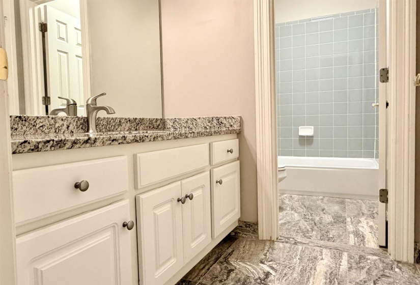 Bathroom featuring a white vanity with a speckled countertop and brushed nickel faucet, a large wall mirror, and grey patterned flooring