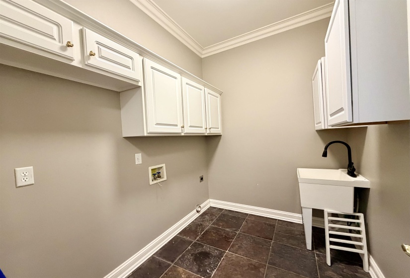 Laundry area featuring white cabinetry, a utility sink with a matte black faucet, and dark-toned square floor tiles