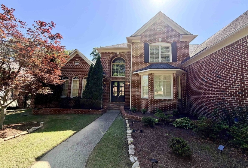 Traditional brick residence featuring a prominent arched entry, bay window with metal awning, and decorative shutters