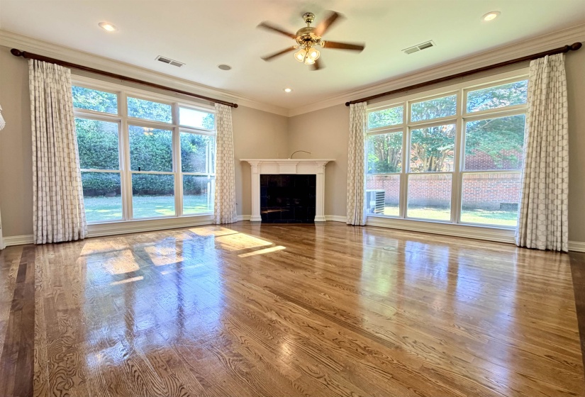 Spacious interior featuring wood-finish flooring with a border inlay, a fireplace with a white mantel, and two large multi-pane windows