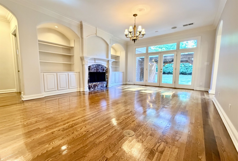 Spacious living area featuring wood-finish flooring, a built-in fireplace with a stone surround, and custom built-in shelving with cabinetry