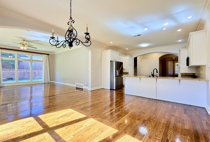 Open-concept eat in area featuring hardwood flooring, extensive crown molding, a kitchen with white cabinetry, stainless steel appliances, and granite countertops, and an arched entryway