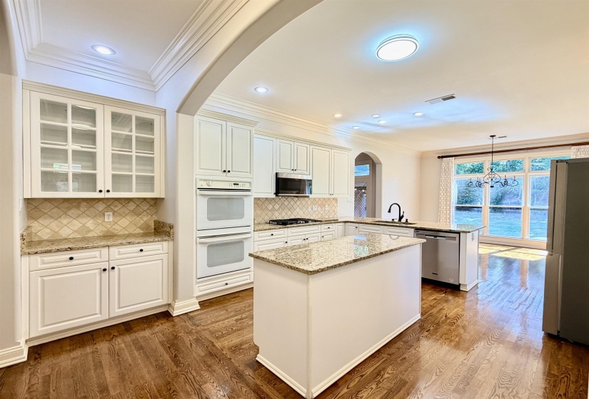 Kitchen featuring white cabinetry, granite countertops, tile backsplash, wood-finish flooring, and stainless steel appliances including double ovens