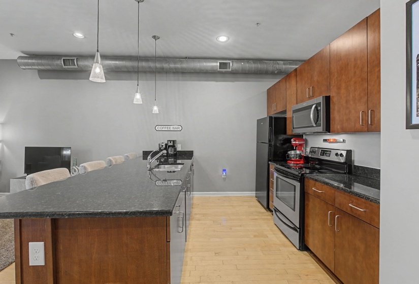 Kitchen featuring a peninsula, stainless steel appliances, a breakfast bar, dark stone countertops, and light wood-style flooring