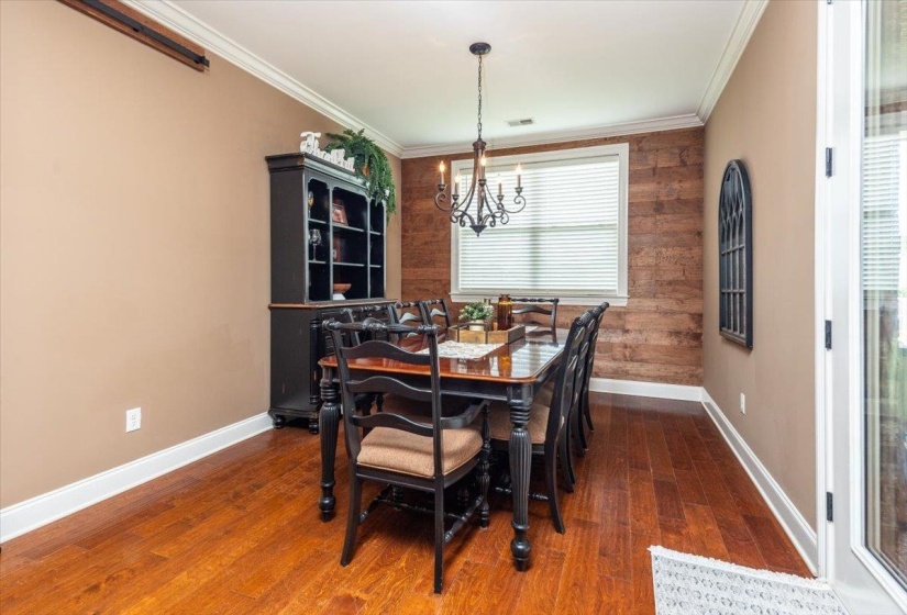 Dining area featuring wood-finish flooring, a rustic wood accent wall, crown molding, and a multi-bulb chandelier