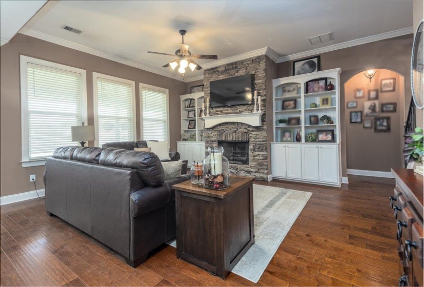 Living area featuring wood-finish flooring, a stone fireplace with a white mantel, and built-in white cabinetry