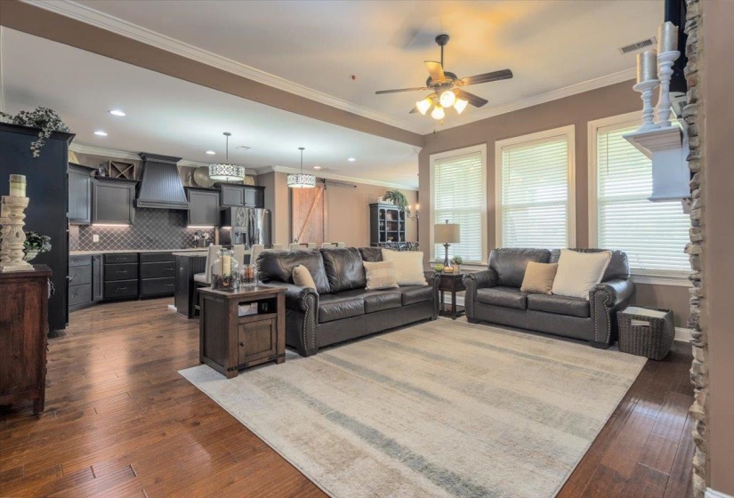 Open-concept living space featuring wood-finish flooring, a contemporary ceiling fan, and multiple windows with blinds