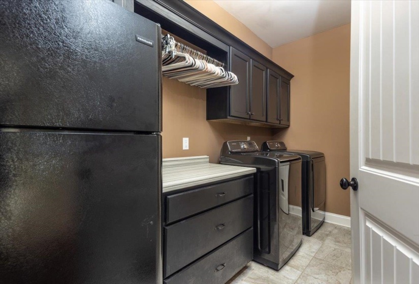 Laundry room featuring black shaker-style cabinetry, a built-in hanging rod, light-toned flooring, and a white beadboard door