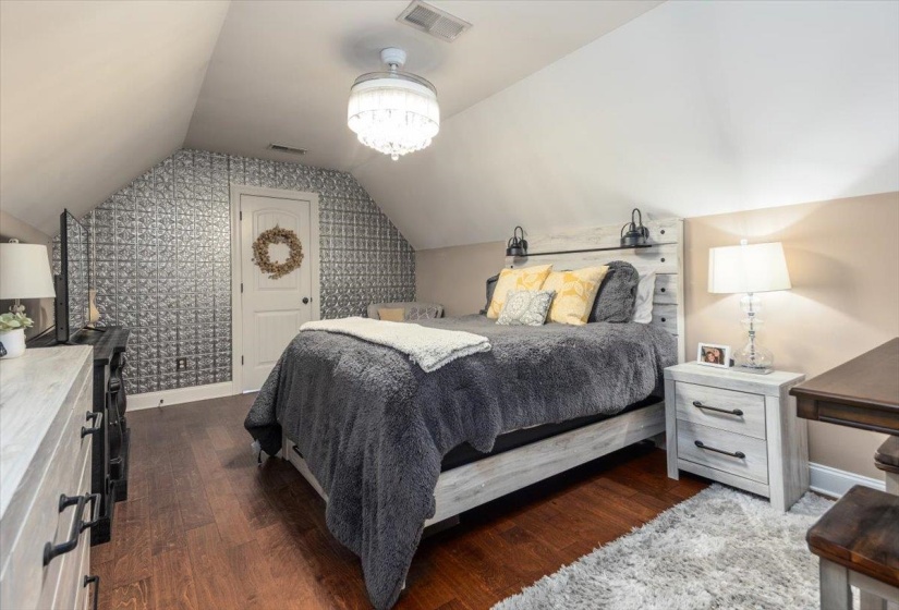 Attic room featuring a sloped ceiling, wood-finish flooring, and a textured wall with a pressed metal pattern