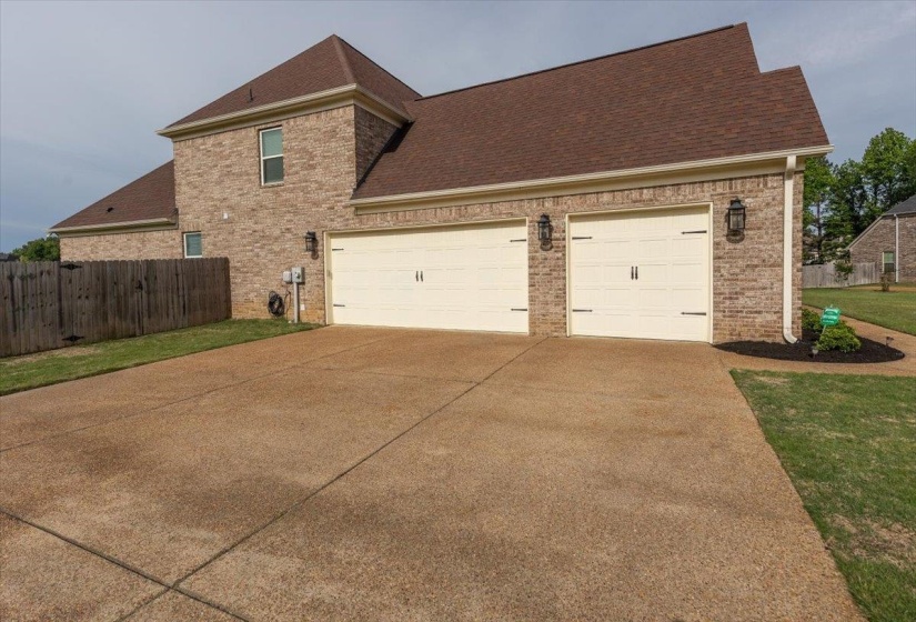 Brick exterior with a brown shingle roof, featuring two carriage-style garage doors with decorative hardware, a concrete driveway, and exterior wall sconces