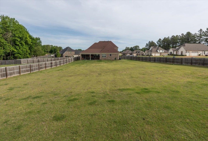 Expansive rear yard featuring a privacy fence, mature perimeter trees, and a brick exterior home with a covered patio