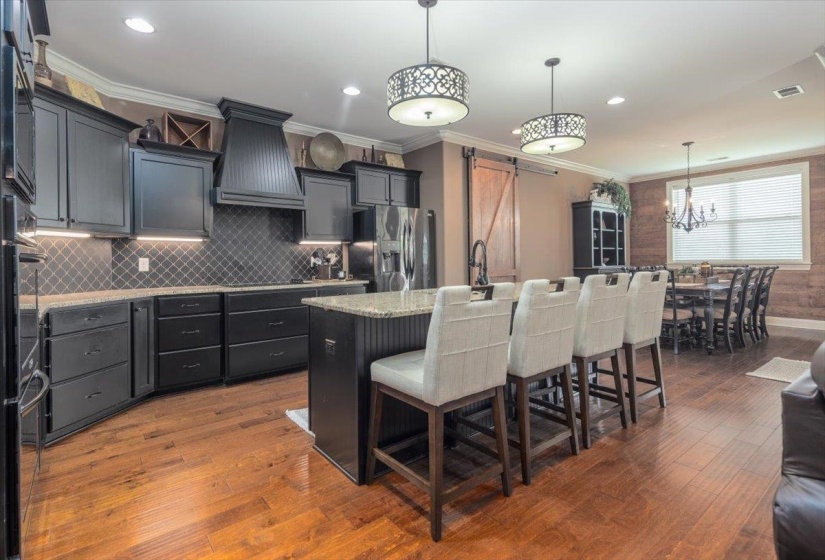 Contemporary kitchen featuring dark cabinetry, granite countertops, a diamond-patterned tile backsplash, and wood-finish flooring
