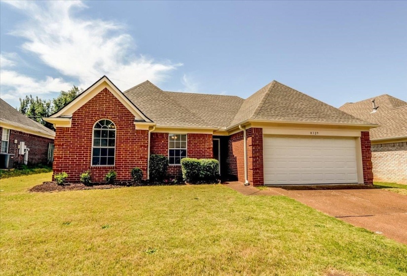 Brick exterior featuring an arched window, a two-car garage, and a gabled roofline
