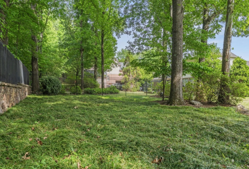 Expansive back yard featuring a stone retaining wall, black metal fencing, and mature trees