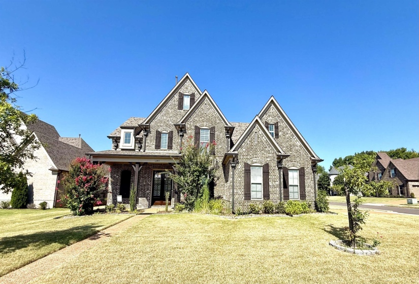 French country home featuring brick siding, a front lawn, and a porch
