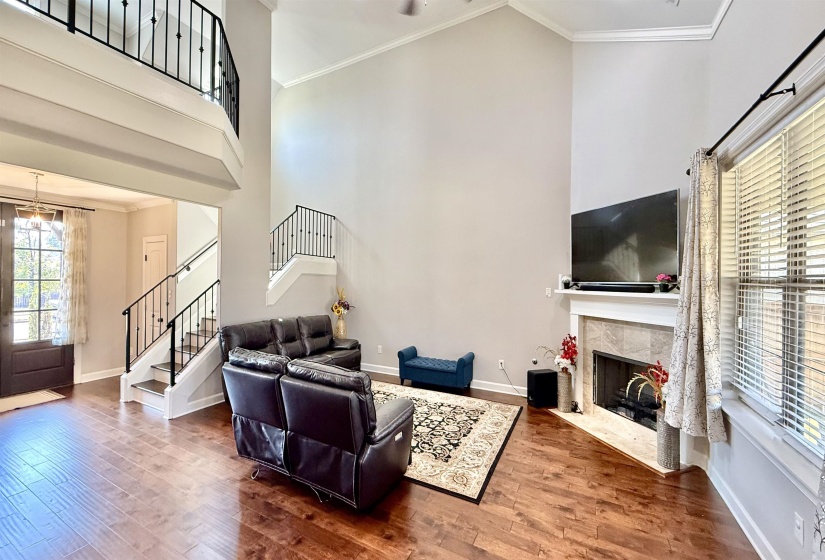 Living room featuring crown molding, a towering ceiling, wood finished floors, a high end fireplace, and stairs