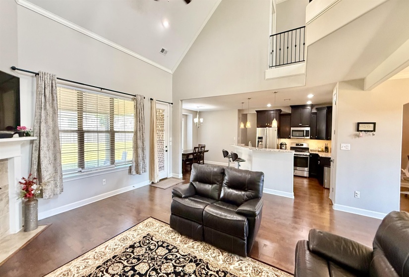 Living room with high vaulted ceiling, a high end fireplace, wood finished floors, a chandelier, and ornamental molding
