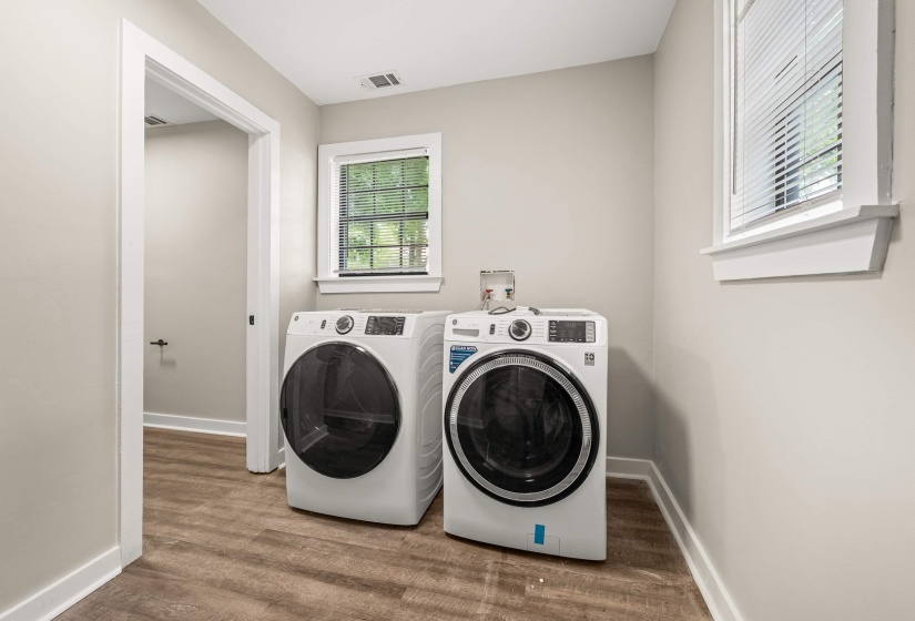 Laundry area featuring wood-finish flooring, light neutral walls, white trim, and a window with blinds