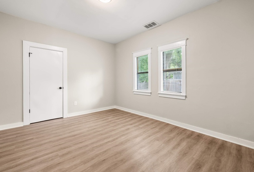 Room featuring wood-finish flooring, two large windows, white trim, a white door with black hardware, and light-toned walls