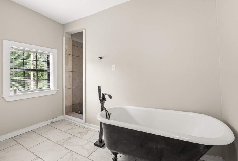 Freestanding clawfoot tub with a matte black floor-mounted faucet, tile flooring, and a walk-in shower with tiled walls