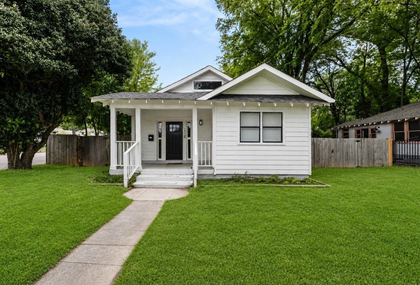 White siding exterior featuring a covered front porch with white railings, a dark paneled front door, and black-framed windows