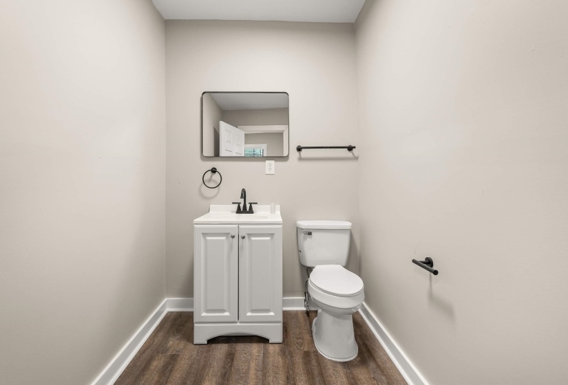 Powder room featuring a white single-sink vanity with cabinet storage, a rectangular mirror, and wood-finish flooring
