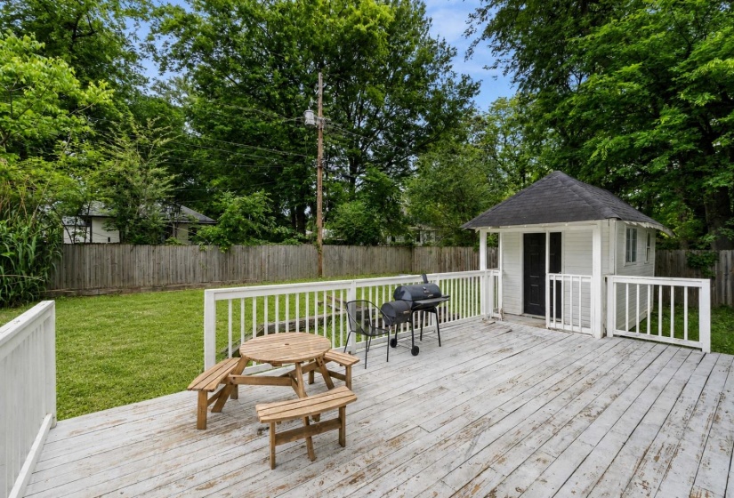 Expansive wood-finish deck with white railing, featuring a detached shed with a dark shingle roof and a private fenced yard