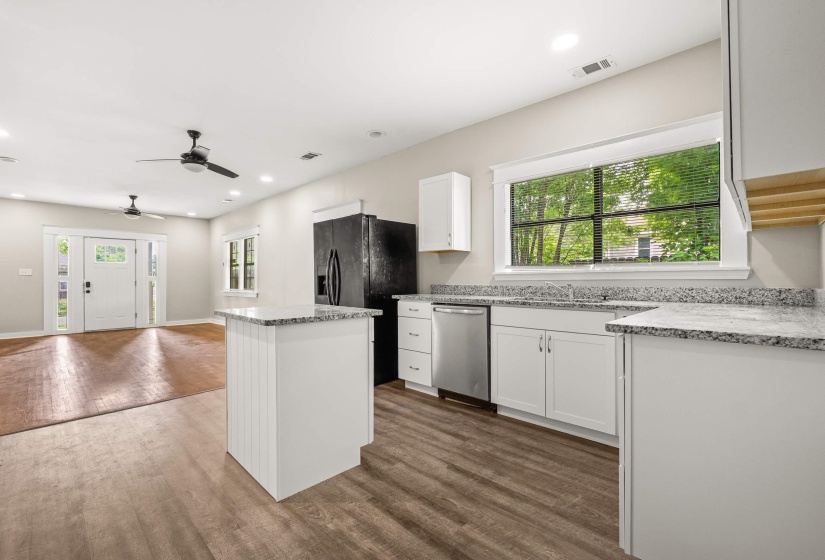 Open-concept kitchen featuring white cabinetry, granite countertops, an island with shiplap-style paneling, stainless steel appliances, and wood-finish flooring