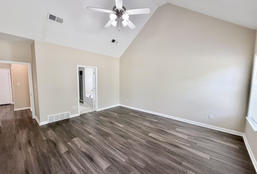 Spacious room featuring vaulted ceilings, a ceiling fan with integrated lighting, wood-finish flooring, and neutral wall tones