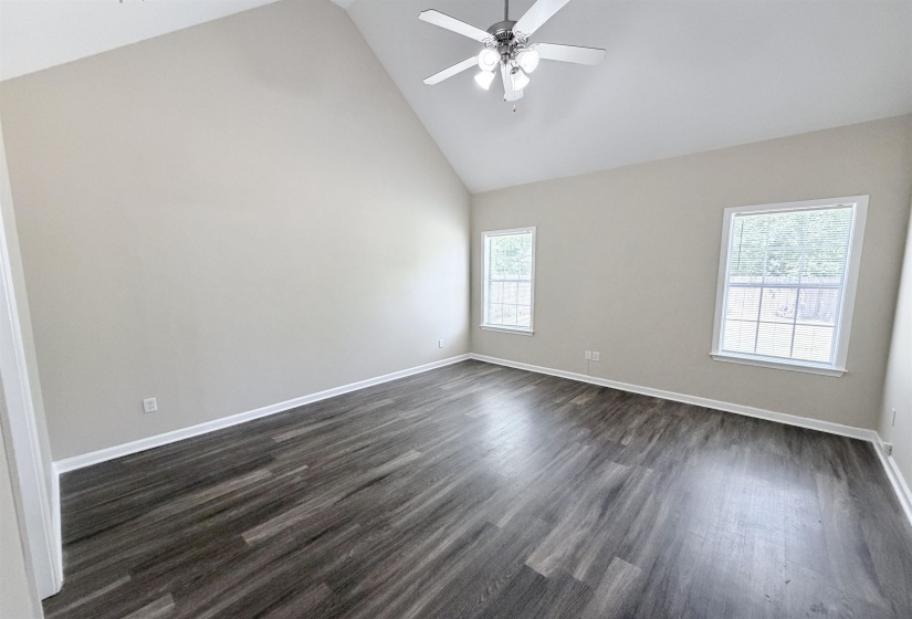 Spacious room featuring a vaulted ceiling with a ceiling fan, two windows, wood-finish flooring, and light-toned walls