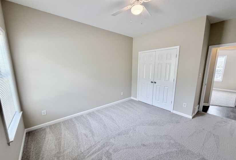 Spacious room featuring neutral carpeting, light-toned wall paint, a built-in double-door closet, a window with blinds, and a ceiling fan with integrated lighting