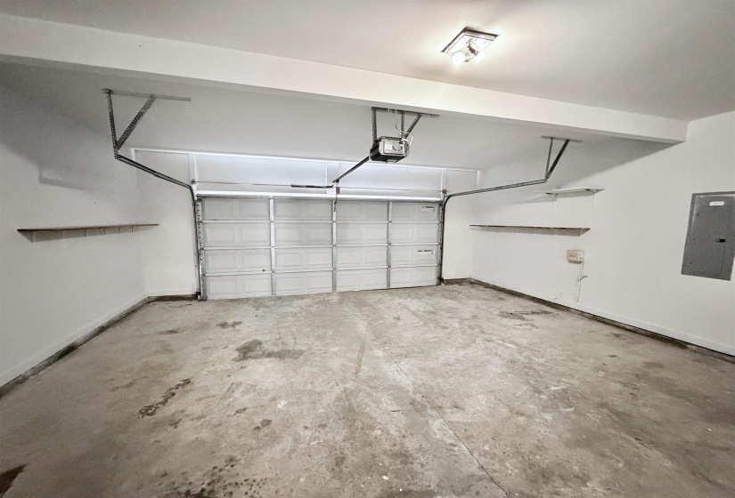 Spacious garage featuring a sectional overhead door, built-in shelving, concrete flooring, overhead lighting, and an electrical panel