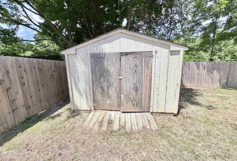 Wood-sided storage shed with double doors and a sloped roof, set within a fenced yard