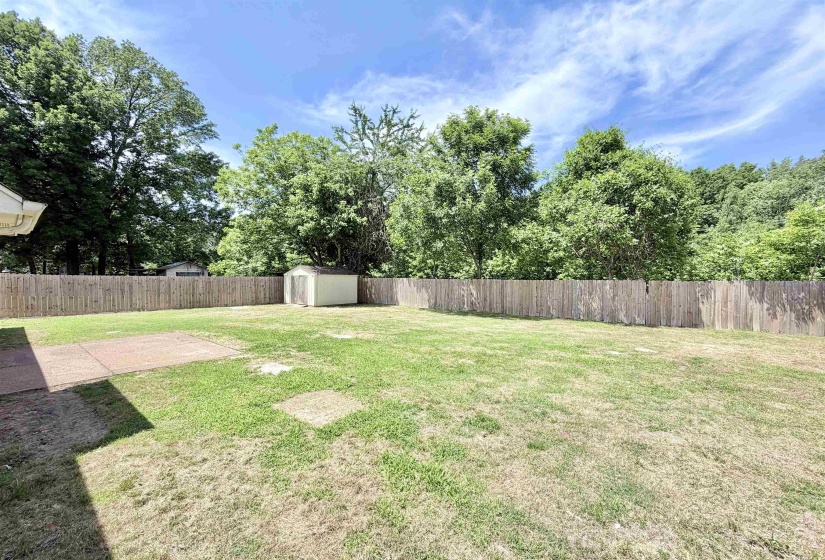 Expansive backyard featuring a wood privacy fence, concrete patio, a storage shed, and mature perimeter trees