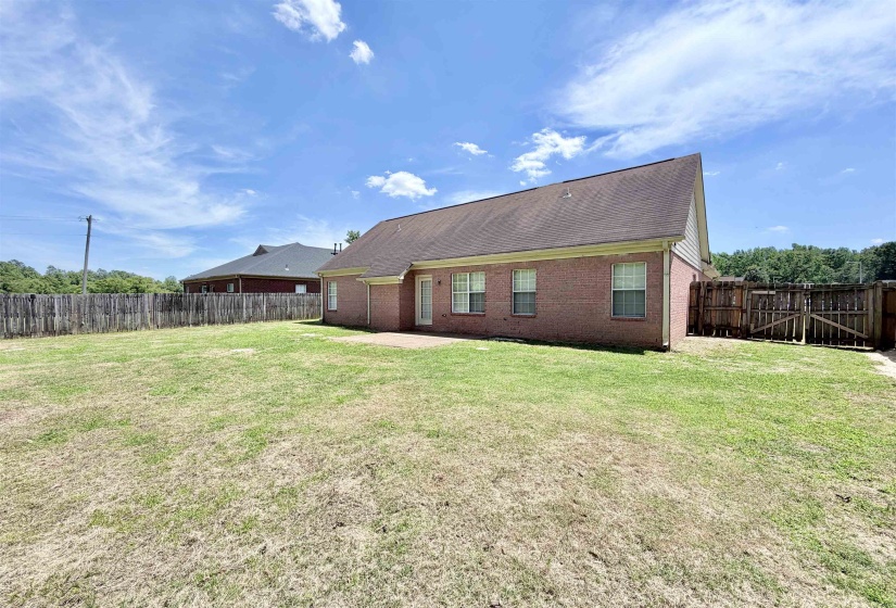 Expansive backyard featuring a brick exterior, multiple windows with white frames, a patio area, and a privacy fence